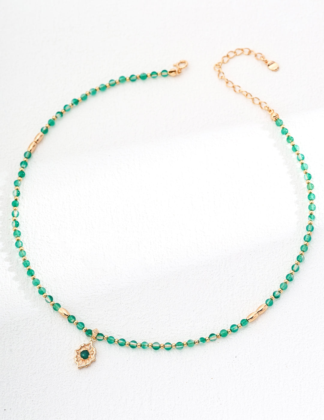 This elegant necklace features green beads and gold accents, with a symbolic gold pendant that holds a green gemstone at the center. The pendant is designed with a healing, lotus-like shape, symbolizing growth and balance. Its adjustable chain makes it a versatile piece, perfect for layering or wearing solo. This is a short length necklace.